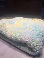 Folded crocheted baby blanket showing pastel tones and thick knitting texture.