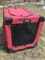 Red soft sided portable dog crate standing outdoors, showing front mesh zippered opening and Nature's Miracle label.