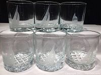 Front view of six Old Fashioned rocks glasses arranged in two rows of three, showing the frosted etched sailboat and buoy design on each glass.