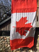 Canadian flag hanging on a wooden wall outside, showing red and white colors with a red maple leaf center.