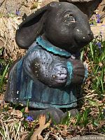 Side view of heavy concrete rabbit statue in grass and garden setting showing detailed paint and wear.