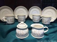 Full view of the tea set including four cups, four saucers, creamer and sugar bowl all decorated with brown branches, white buds, and gold trim