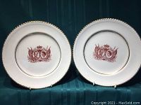 Pair of white plates with red portrait decals of Queen Elizabeth and Prince Philip on top of a dark green fabric background