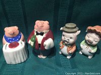 Two pairs of vintage ceramic pig salt and pepper shakers, displayed side by side on a dark teal textured surface.