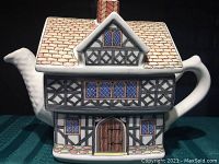 Front view of Tudor house teapot shaped as a ceramic collectible with detailed windows and wooden door design.