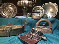 Wide view showing assortment of metal decorative pieces, sad irons, hole punch, and trays on blue cloth background