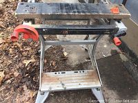 Full view of used Jobmate sawhorse with black metal swing arm, orange handles, and metal frame showing wear and use.