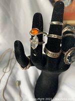 Multiple silver rings displayed on a black velvet hand jewelry holder including stones and different patterns.