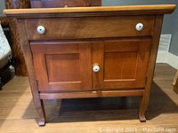 Front view of vintage maple bedside table showing drawer with two white knobs and two cabinet doors below.