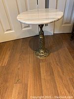 Full view of the side table showing the round white marble top and the decorative hollow metal base with intricate cut-out designs.
