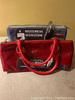 Red crocodile embossed insulated wine bag standing in front of glittery insulated wine bag with visible label and zipper