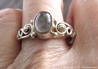 Ring worn on finger showing the oval moonstone cabochon and silver band with figure 8 and bead details.