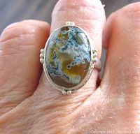 Close-up of ring worn on finger showcasing moss agate stone and silver beaded frame.