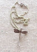 Top view of vintage sterling silver dragonfly pendant on silver chain laid on fabric.