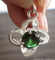 Front close-up of silver pendant showing emerald-colored round faceted stone in prong setting.