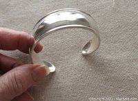 Hand-held photo showing polished sterling silver Silpada bangle with smooth reflective surface and tapered design