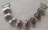 Front view showing all 8 links of the bracelet with distinct Peruvian tribal mask designs, silver with raised and stamped details.