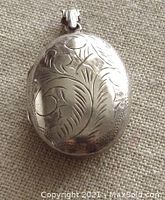 Exterior view of the silver oval locket showing detailed floral engravings and the engraved bail.