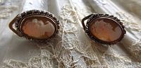 Front view of both oval shell cameo clip on earrings showing the carved female profiles and twisted silver frames.