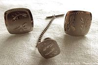 Front view of two square sterling silver cuff links and one matching tie tac, showing engraved floral or leaf pattern and polished finish.