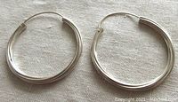 Pair of large twisted hoop earrings laid flat on cloth, showing shape and texture