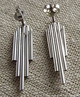Pair of silver tubular earrings laid on fabric background, showing front view of design and post backs