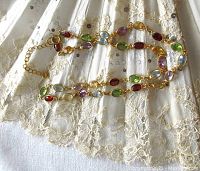 Full view of entire gold-washed sterling silver necklace with multi-color bezel set gemstones on lace background.