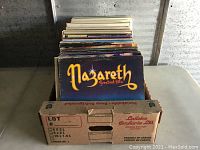 Front view of the vinyl record lot showing approximately 50 LPs upright in a cardboard box. The frontmost visible album is 'Nazareth Greatest Hits' with a worn cover.