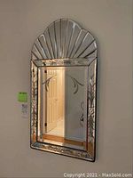 Full view of the vintage wall mirror hung on a light-colored wall showing the fan-shaped top and floral etched border.