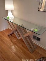 Full side view of the console table showing the wooden criss-cross base and clear glass top with rounded corners.