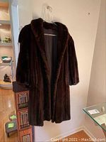 Full view of dark brown mink fur coat hanging on a hanger showing the shawl collar and overall length.