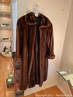 Full front view of brown mink fur coat hanging on hanger showing length and collar.