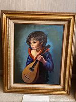 Front view of the oil painting showing a boy holding a mandolin, framed.