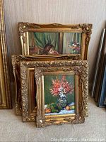 Four paintings stacked against wall, showcasing ornate gold frames and visible art details