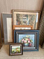 Full view of the 5 framed wall art pieces stacked leaning against a wall showing variety in sizes and frames.