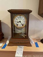 Full front view of bronze mantel clock on wooden table with labels beneath