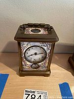 Front view of carriage clock showing porcelain dial and front panel with pastoral scene of couple under trees