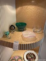 Display shelf with green Murano bowl, clear wavy rim trinket dish, clear glass bowl, and small perfume bottles in corner
