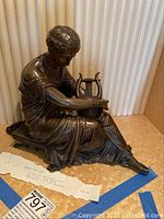 Front view showing the full seated bronze figure holding a lyre with visible fine details of the figure's hair and dress.