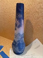 Full side view of tall slender cameo glass vase with blue and white landscape scene on wood background with appraisal document partially visible