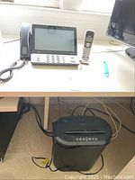 Desk with CapTel Bluetooth phone model 2400BT featuring large screen and wired handset on the left, and Uniden cordless phone with base on the right. Under the desk is a black Omnitech paper shredder.