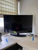 Front view of Samsung 31-inch TV on stand placed on a white desk with blue tape markers nearby.
