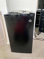 Front view of black Igloo mini-fridge showing scratches and single door with Igloo logo on the top right corner.