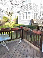 Photo showing four rectangular rail-fitted plastic planters attached to wooden deck railings, weathered with dirt and some plant debris inside.