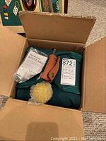 Open cardboard box with bocce ball set, instruction manual, and accessories inside.