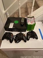 Full view of original Xbox console, three wired controllers, remote, and eight Xbox game cases.