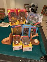 Overall view of sports figurines and memorabilia on pool table, showing boxed basketball figures, baseball bookends, baseball, and home run alarm clock.