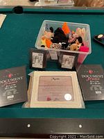 Photo showing the plastic bin filled with assorted Beanie Babies and two black document frames on each side of a white framed 'Mom' poem plaque on a pool table.