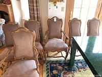 Wide angle photo showing all six dining chairs, two with armrests (captains) and four side chairs (mates) gathered around a dining table, wood carved frames, beige upholstery.