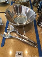 Photo shows the Nambe metal salad bowl and two long salad forks in polished metal, placed on a table with measuring tape visible